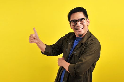 Happy of young Asian man smiling and giving thumbs up, copy space, isolated on yellow background