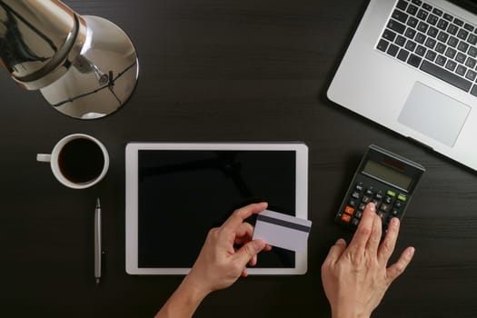 Internet shopping concept.Top view of hands working with laptop and credit card and tablet computer on dark wooden table background
