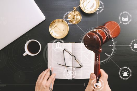 justice and law concept.Top view of Male judge hand in a courtroom with the gavel and brass scale and computer and open bible book on dark wood table with Vr diagram