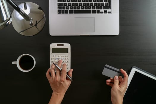 Internet shopping concept.Top view of hands working with calculator and laptop and credit card and tablet computer on dark wooden table background