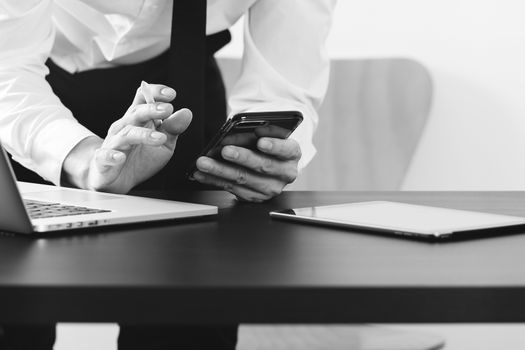 close up of businessman working with smart phone and digital tablet and laptop computer on wooden desk in modern office ,black and white