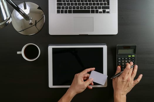 Internet shopping concept.Top view of hands working with calculator and laptop and credit card and tablet computer on dark wooden table background