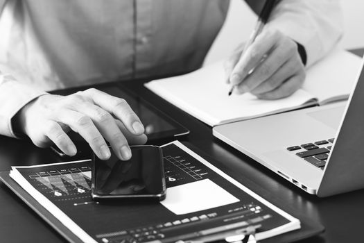 close up of businessman working with smart phone and digital tablet and laptop computer  on wooden desk in modern office,black and white