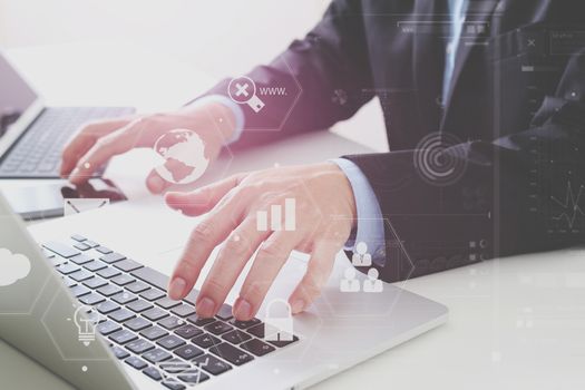 Hands of businessman typing on laptop in modern office with smart phone and digital tablet computer with VR icon diagram