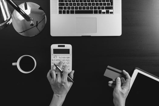 Internet shopping concept.Top view of hands working with calculator and laptop and credit card and tablet computer on dark wooden table background,black and white