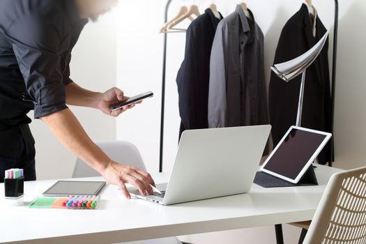 Fashion designer working with mobile phone and using laptop with digital tablet computer in modern studio 