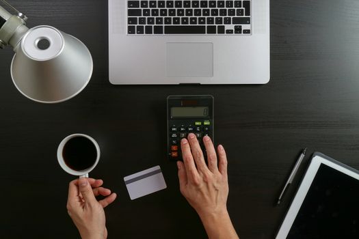 Internet shopping concept.Top view of hands working with calculator and laptop and credit card and tablet computer on dark wooden table background