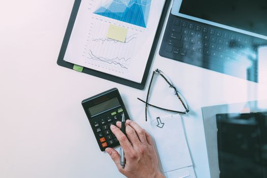 top view of businessman hand working with finances about cost and calculator and latop with mobile phone on withe desk in modern office 