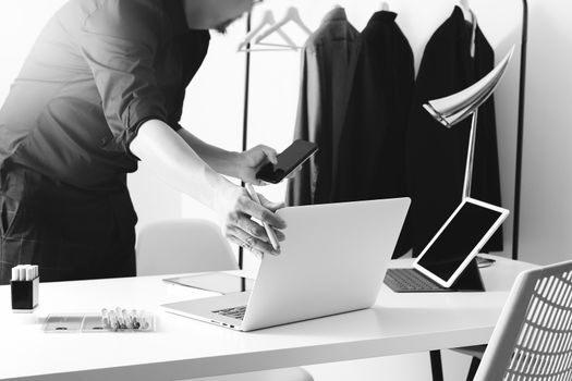 Fashion designer working with mobile phone and using laptop with digital tablet computer in modern studio,black and white