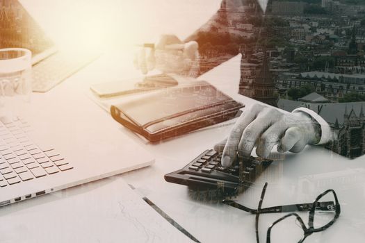 businessman hand working with finances about cost and calculater and latop with mobile phone on withe desk in modern office with city exposure