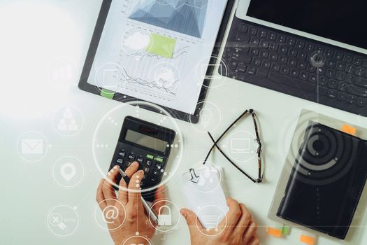 top view of businessman hand working with finances about cost and calculator and latop with mobile phone on withe desk in modern office with VR icon diagram