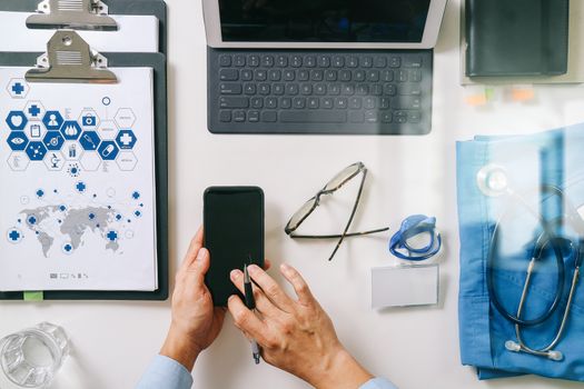 top view of smart medical doctor working with mobile phone and laptop computer and stethoscope on dark wooden desk 