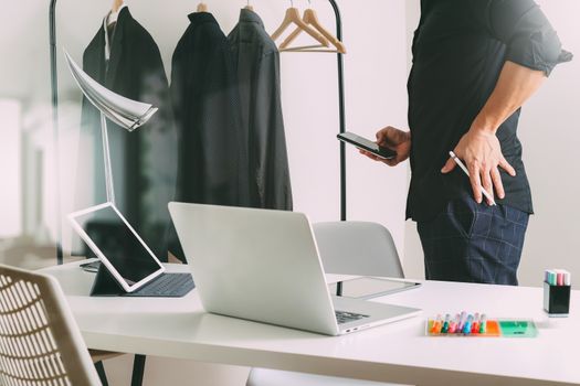 Fashion designer talking mobile phone and using laptop with digital tablet computer in modern studio 