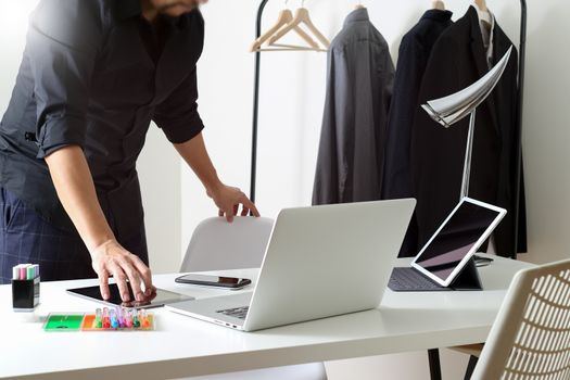 Fashion designer talking mobile phone and using laptop with digital tablet computer in modern studio 