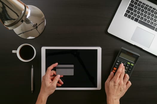 Internet shopping concept.Top view of hands working with laptop and credit card and tablet computer on dark wooden table background