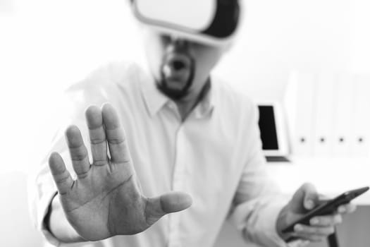 businessman wearing virtual reality goggles in modern office with mobile phone using with VR headset,black and white