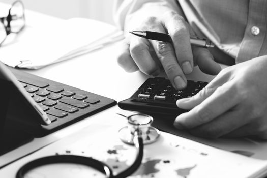 Healthcare costs and fees concept.Hand of smart doctor used a calculator for medical costs in modern hospital ,black and white