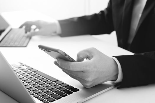 Hands of businessman using mobile phone in modern office with laptop and digital tablet computer ,black and white