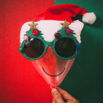 Hand holding Christmas glasses that decoration with Christmas tree and red hat on air bolloon   on green background