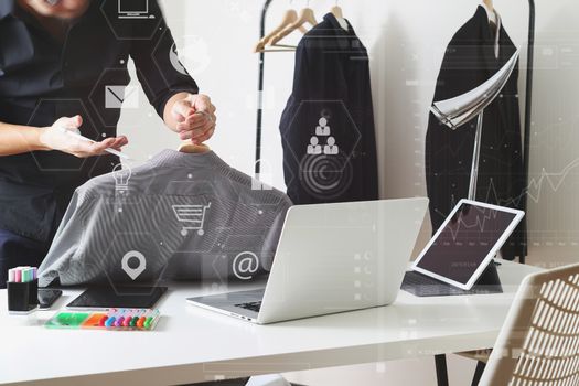 Fashion designer holding shirt and using laptop with digital tablet computer in modern studio with VR icon diagram