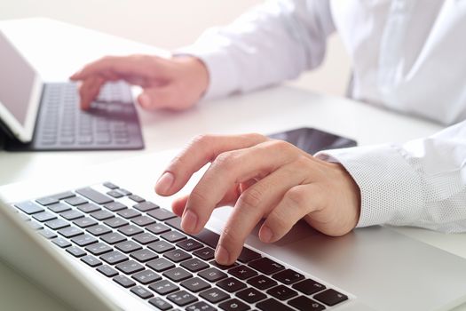 close up of businessman typing digital tablet with keyboard and laptop computer on white desk in modern office