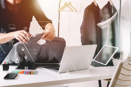 Fashion designer holding shirt and using laptop with digital tablet computer in modern studio with VR icon diagram