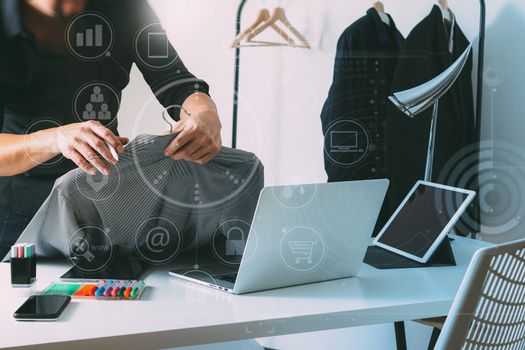 Fashion designer holding shirt and using laptop with digital tablet computer in modern studio with VR icon diagram