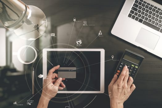 Internet shopping concept.Top view of hands working with laptop and credit card and tablet computer on dark wooden table background with Vr diagram