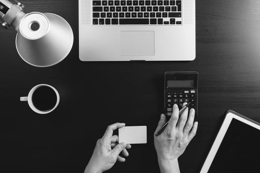 Internet shopping concept.Top view of hands working with calculator and laptop and credit card and tablet computer on dark wooden table background,black and white