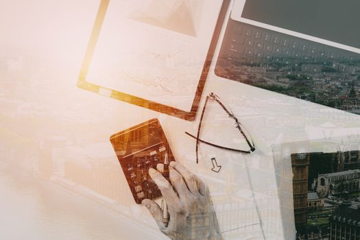 top view of businessman hand working with finances about cost and calculator and latop with mobile phone on withe desk in modern office with buildings exposure 