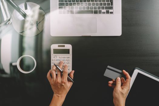 Internet shopping concept.Top view of hands working with calculator and laptop and credit card and tablet computer on dark wooden table background