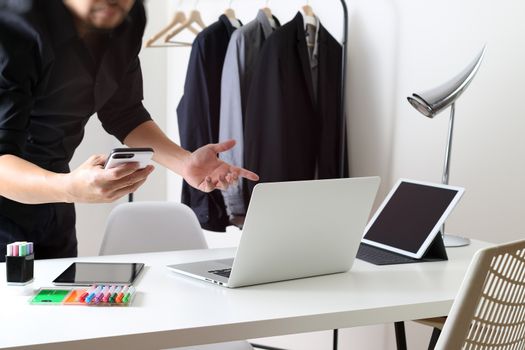 Fashion designer talking mobile phone and using laptop with digital tablet computer in modern studio