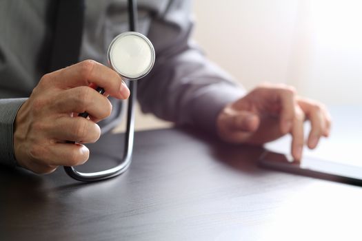 close up of smart medical doctor working with stethoscope and mobile phone on dark wooden desk in modern hospital 