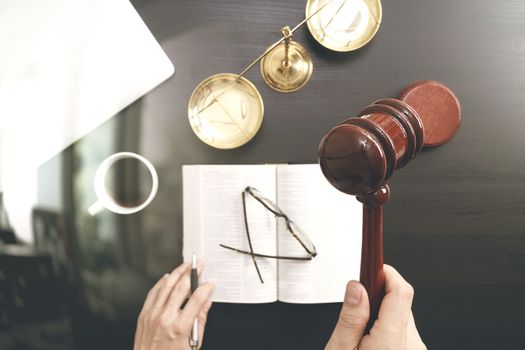 justice and law concept.Top view of Male judge hand in a courtroom with the gavel and brass scale and computer and open bible book on dark wood table 