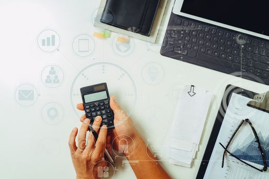 top view of businessman hand working with finances about cost and calculator and latop with mobile phone on withe desk in modern office with VR icon diagram