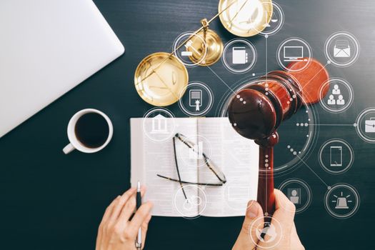 justice and law concept.Top view of Male judge hand in a courtroom with the gavel and brass scale and computer and open bible book on dark wood table with Vr diagram