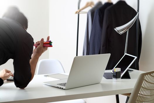 Fashion designer working with mobile phone and using laptop with digital tablet computer in modern studio with city exposure