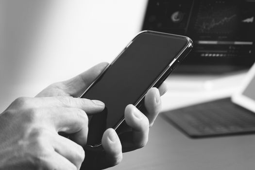 close up of businessman hand working with mobile phone and laptop and digital tablet computer in modern office,black and white 