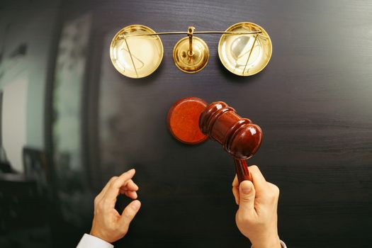 justice and law concept.Top view of Male judge hand in a courtroom with the gavel and brass scale on dark wood table