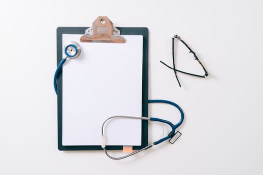 blank stethoscope and gray clipboard and eyeglasses on white desk background