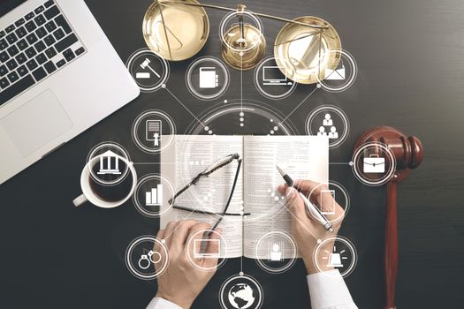 justice and law concept.Top view of Male judge hand in a courtroom with the gavel and brass scale and computer and open bible book on dark wood table with Vr diagram