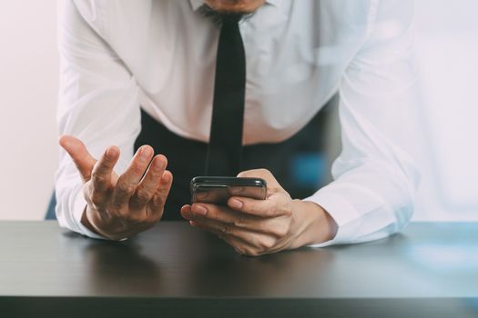 close up of businessman working with smart phone on wooden desk in modern office with glass reflected view