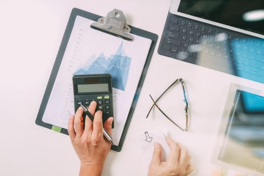 top view of businessman hand working with finances about cost and calculator and latop with mobile phone on withe desk in modern office 