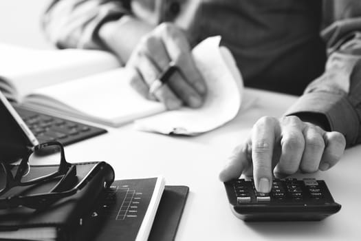 businessman hand working with finances about cost and calculator and latop with mobile phone on withe desk in modern office,black and white