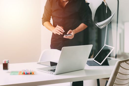 Fashion designer working with mobile phone and using laptop with digital tablet computer in modern studio 