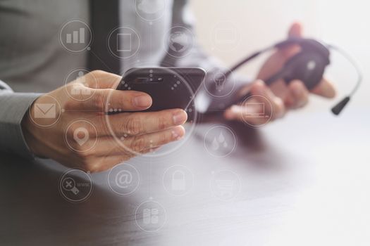 businessman using VOIP headset with mobile phone and concept communication call center on wooden desk with virtual reality icon diagram