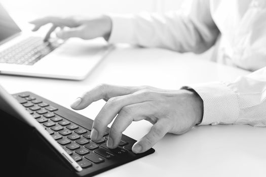 close up of businessman typing keyboard with laptop computer and digital tablet on white desk in modern office,black and white