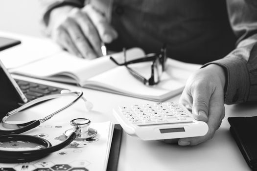 Healthcare costs and fees concept.Hand of smart doctor used a calculator for medical costs in modern hospital,black and white