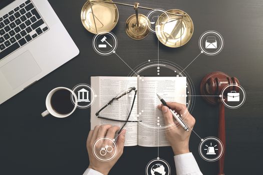 justice and law concept.Top view of Male judge hand in a courtroom with the gavel and brass scale and computer and open bible book on dark wood table with Vr diagram