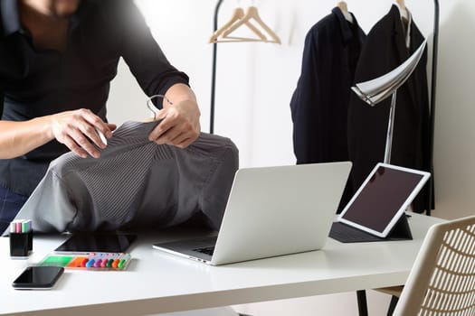 Fashion designer holding shirt and using laptop with digital tablet computer in modern studio 